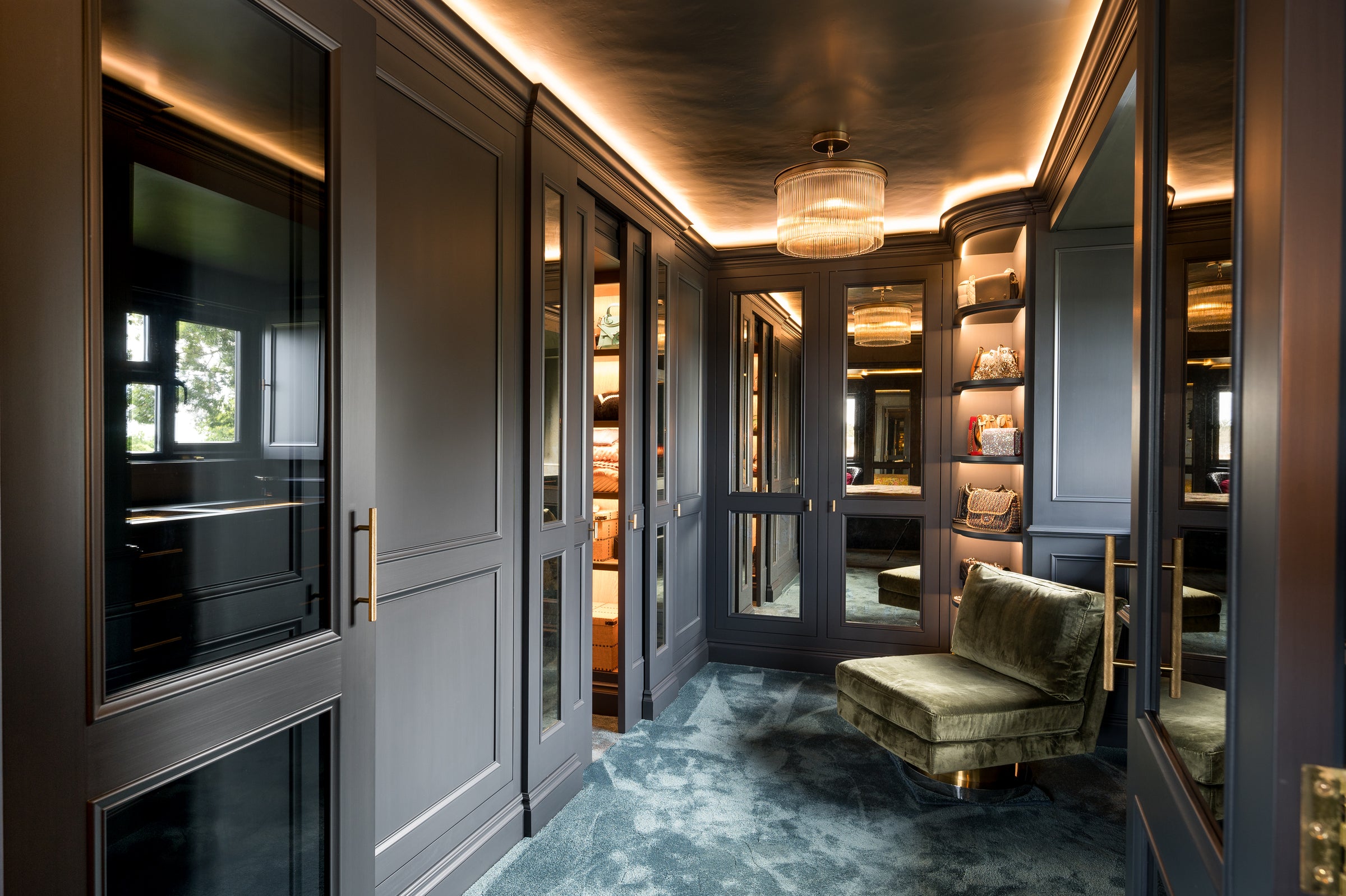 Luxurious interior with dark wood paneling, a green velvet chair, and shelves filled with books and decor.